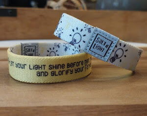 A yellow bracelet with the words " light shine before you and glory your feet ".